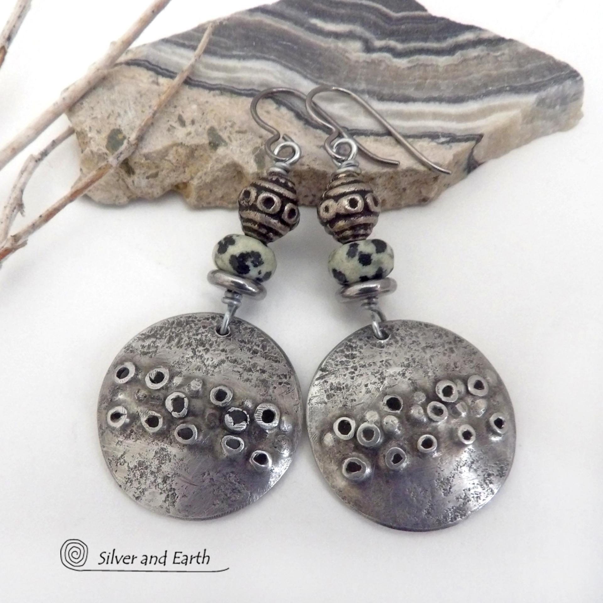 These handcrafted silver pewter earrings have a rustic, hand textured design and are accented with natural dalmatian jasper gemstones, stainless steel and vintage silver tone metal beads. They have an earthy, edgy organic style that makes a unique statement.This type of jasper is known for its spotted pattern that resembles the Dalmatian breed of dog. The matrix consists of mineral inclusions of brown iron oxide, black tourmaline & other minerals which create the natural "spots" in the stone. Handmade in th