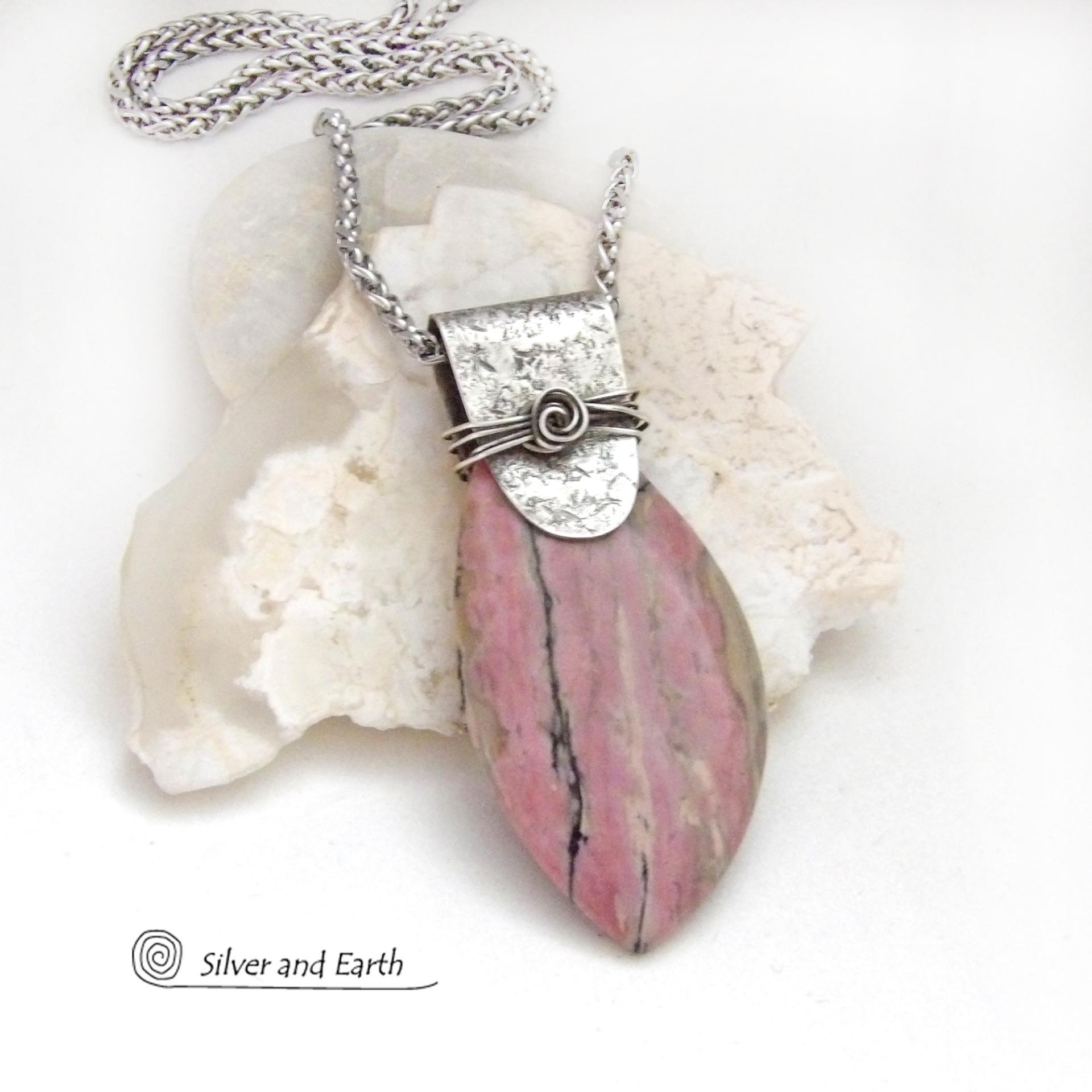 This one-of-a-kind necklace features a large gorgeous rhodonite gemstone accented with a handcrafted sterling silver bail. The stone has a beautiful pink hue with a natural matrix pattern of black, white and tan lines. Coordinating earrings sold separately. Makes a great gift for a natural stone lover - or a nice addition to 