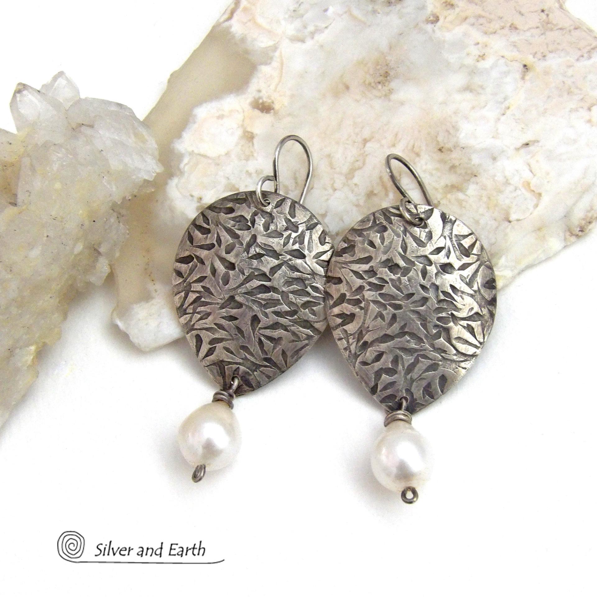 Perfect for everyday wear, these handcrafted sterling silver earrings are accented with dangling white freshwater pearls. The silver has an intricate hand stamped texture with an oxidized finish. The pearls contrast beautifully against the silver metal. They have an elegant, feminine feel with a contemporary design that looks great with all wardrobe styles. They'll make a great gift for someone born in June. Pearl is the traditional gemstone for this month. Handmade in the USA by Silver and Earth Jewelry. 