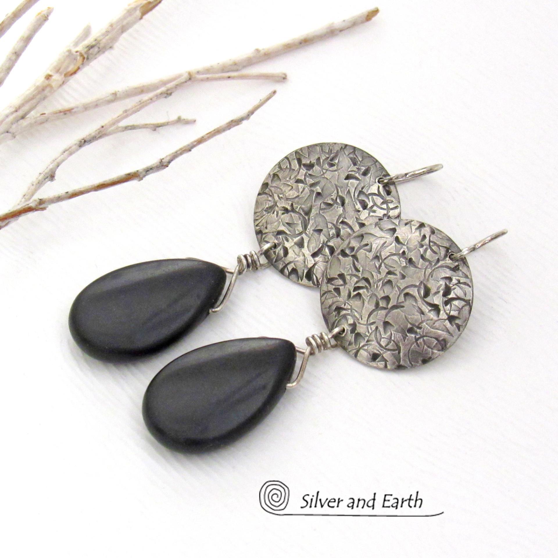 These handcrafted sterling silver earrings have a hand stamped texture and feature dangling black onyx teardrop-shaped gemstones. They have a contemporary modern style with a bold urban chic flair that coordinates beautifully with all wardrobe types.
