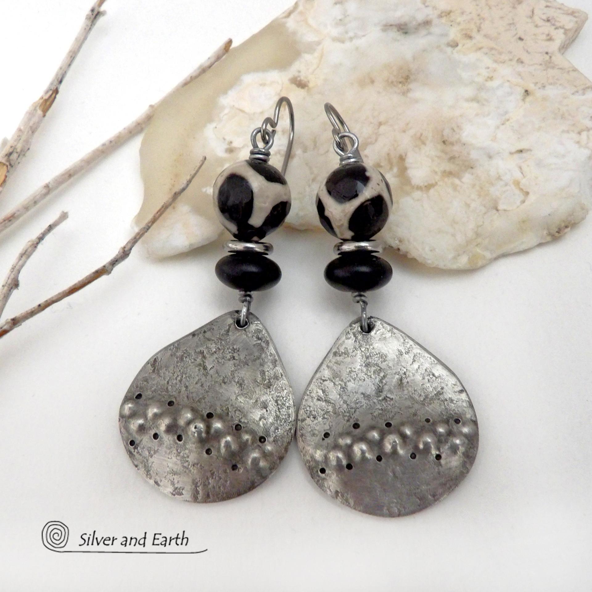These handcrafted silver pewter earrings have a rustic, hammered texture and are accented with black and off-white Tibetan agate faceted gemstones, black glass and stainless steel beads. Bold and striking, they'll make a unique ethnic tribal statement. Perfect for women that love to wear unique, eye-catching jewelry. Handmade in the USA by Silver and Earth Jewelry.  MEASUREMENTS: Total length of approximately 2-1/2" from top of silver niobium (hypoallergenic) ear wires and 1” at widest point.