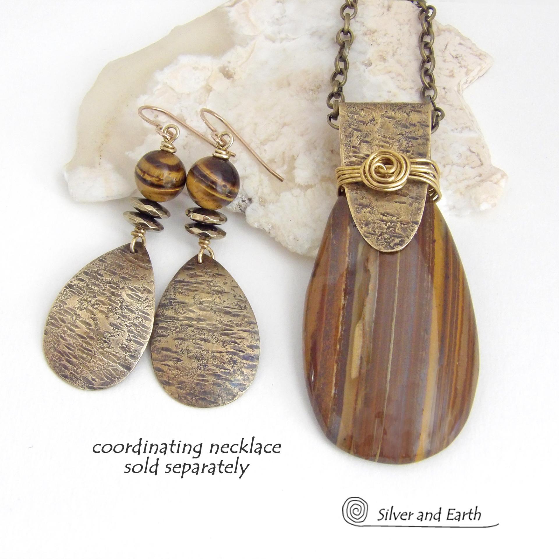 These handcrafted earrings feature textured gold brass teardrop dangles accented with natural brown tiger's eye gemstones and hematite stone beads. The beads have an electroplated champagne gold tone finish which adds a touch of shimmer and shine. They have an earthy modern style that coordinates well with all wardrobe styles. A matching necklace is availabe and sold separately. Handmade in the USA by Silver and Earth Jewelry.