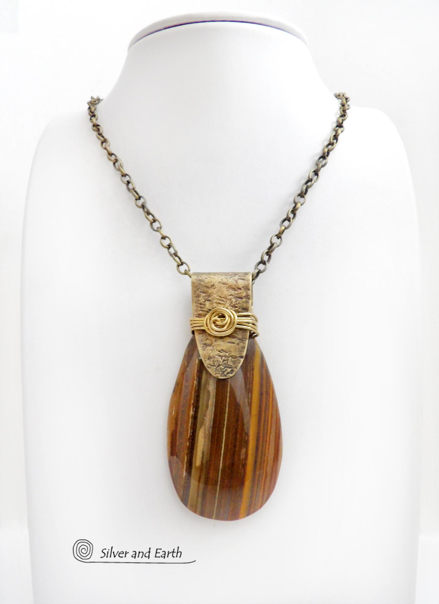 This handcrafted necklace features a natural brown tiger's eye gemstone accented with a gold brass bail. The stone has a beautiful matrix with earthy hues of brown and golden streaks. It has an earthy, modern style that coordinates beautifully with all wardrobe types. Unique and one of a kind, it makes a great gift for a natural stone lover - or a nice addition to your own jewelry collection.
