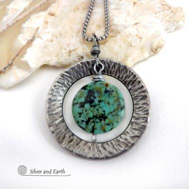 This handcrafted pendant necklace features a natural coin-shaped African turquoise gemstone framed against a hammered and oxidized silver tone pewter circle. It has a modern earthy organic style that coordinates well with all wardrobe types. The design is versatile and can be worn by either a man or woman. It will make a great gift for anyone that loves natural stone jewelry. Handmade in the USA by Silver and Earth Jewelry. 