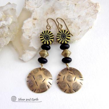 These handcrafted earrings have an ethnic boho tribal vibe. They feature gold brass dangles with a hand stamped spiral and line texture accented with black and light yellow Fimo clay beads with a spiral design, black glass and brass beads. Unique and fun to wear - they have a funky bohemian vibe that makes a bold, striking statement. Perfect for women that love to wear one-of-a-kind artisan handcrafted jewelry. Handmade in the USA by Silver and Earth Jewelry. 